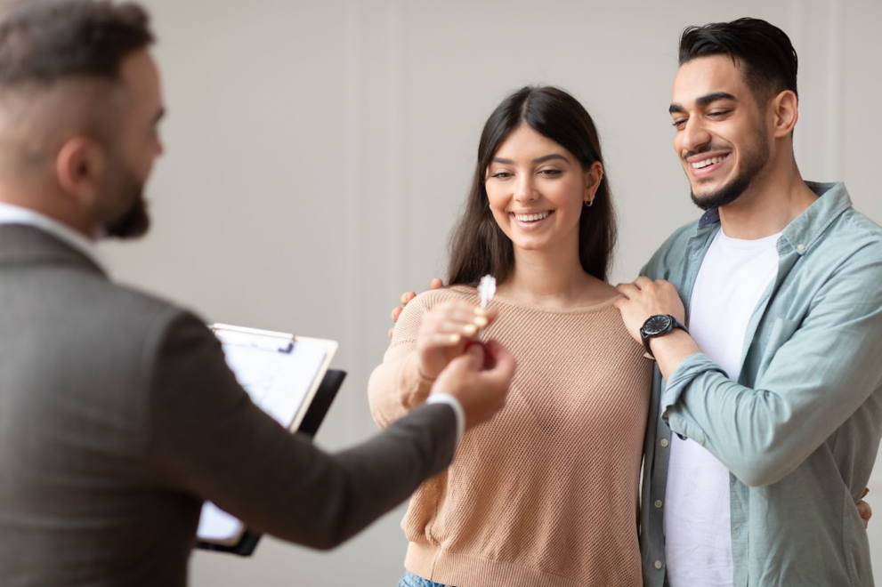 A real estate agent hands over a key to new homeowners after they've closed on a house. Buyers can expect to pay a certain portion of closing costs.
