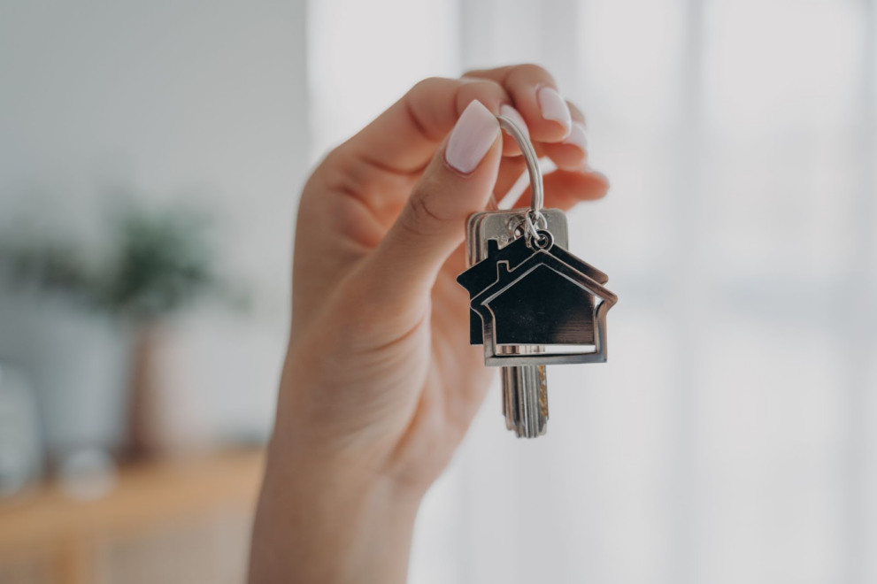 Hand with nail polish holding keys with house-shaped keychains, symbolizing a family member buying a parents house through an arm's length transaction, involving house inspection and transfer pricing to save money and avoid capital gains taxes
