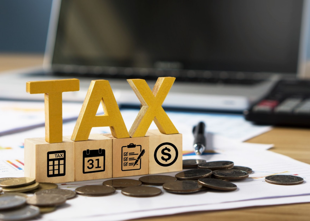 TAX letters on blocks with tax-related icons, laptop, and coins on paper reports, illustrating gift of equity and taxable income considerations in buying a house from a family member with real estate agent assistance, house inspection, and homeowners association fees involved