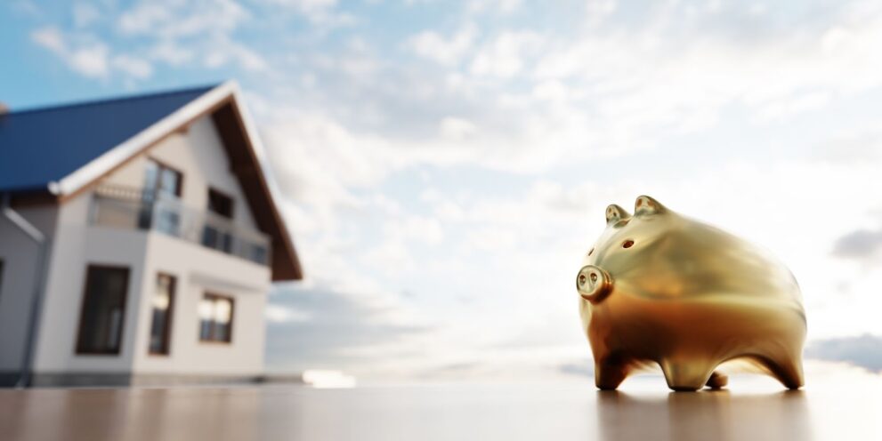 A piggy bank next to a new house, symbolizing saving for a home mortgage