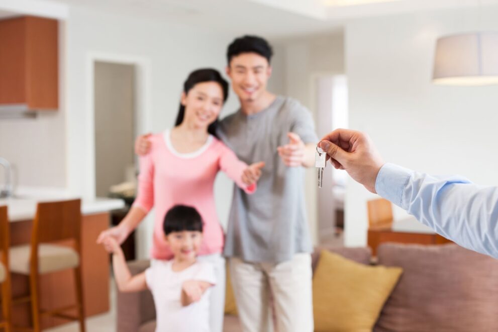 A family of three extend their hands to receive a key being handed to them.