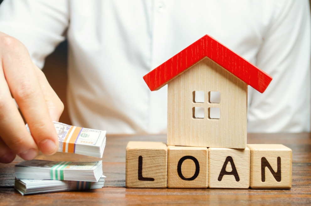 Loan wooden blocks with a toy house over it and paper currencies on the left denoting the lender