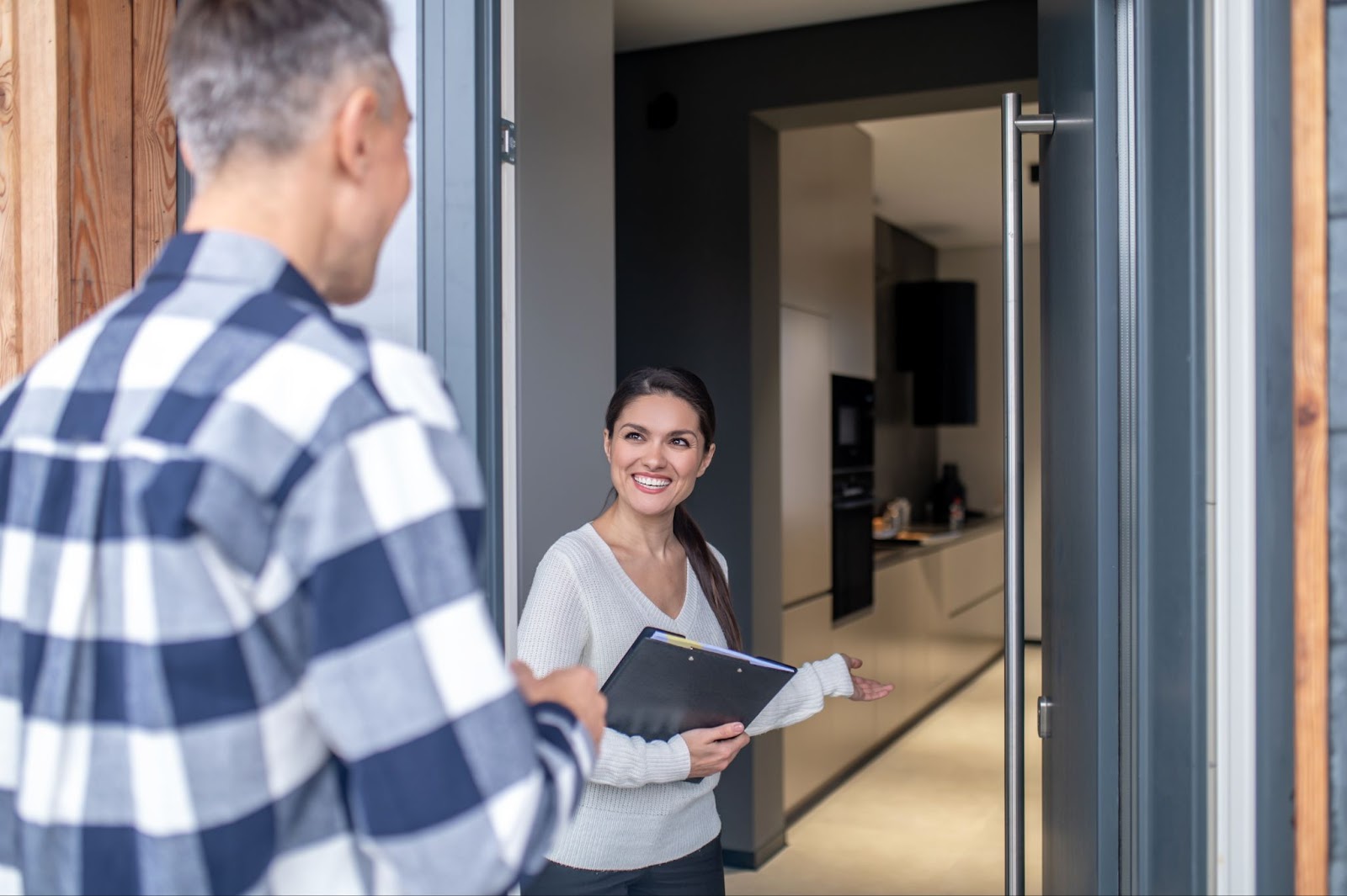 a woman realtor standing at the door of a home talking to a seller